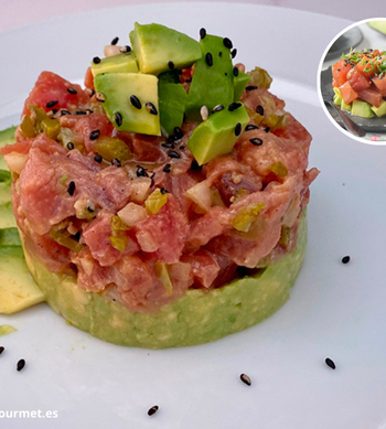 Tartar de atún con aguacate presentado en forma de torre, con dados de atún marinado, aguacate, sésamo y cebollino sobre plato blanco