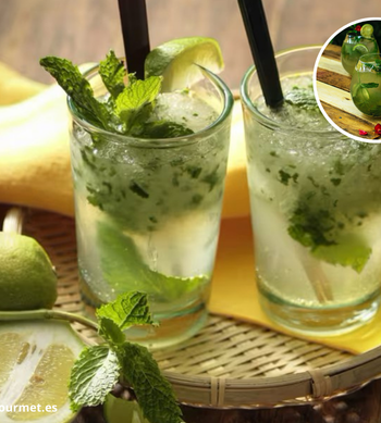 Cóctel Mojito en vaso alto con ron blanco, lima troceada, hojas de menta, hielo y soda, decorado con menta fresca