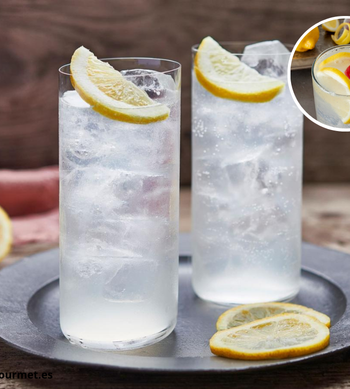 Cóctel Tom Collins con ginebra, limón, soda y hielo en vaso alto decorado con rodaja de limón y cereza.