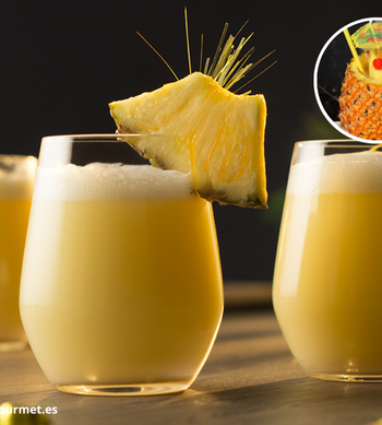 Cóctel Piña Colada en vaso alto con hielo, preparado con ron, crema de coco y piña, decorado con fruta tropical y sombrilla